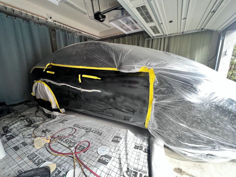 Black sedan masked with plastic sheeting inside a customer garage