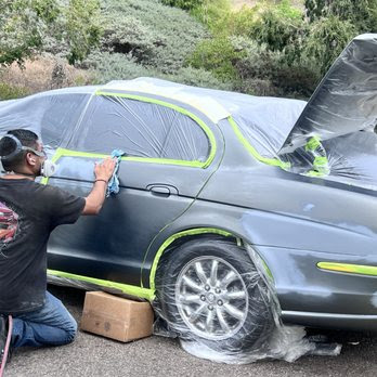 Technician in a respirator painting a gray sedan fender