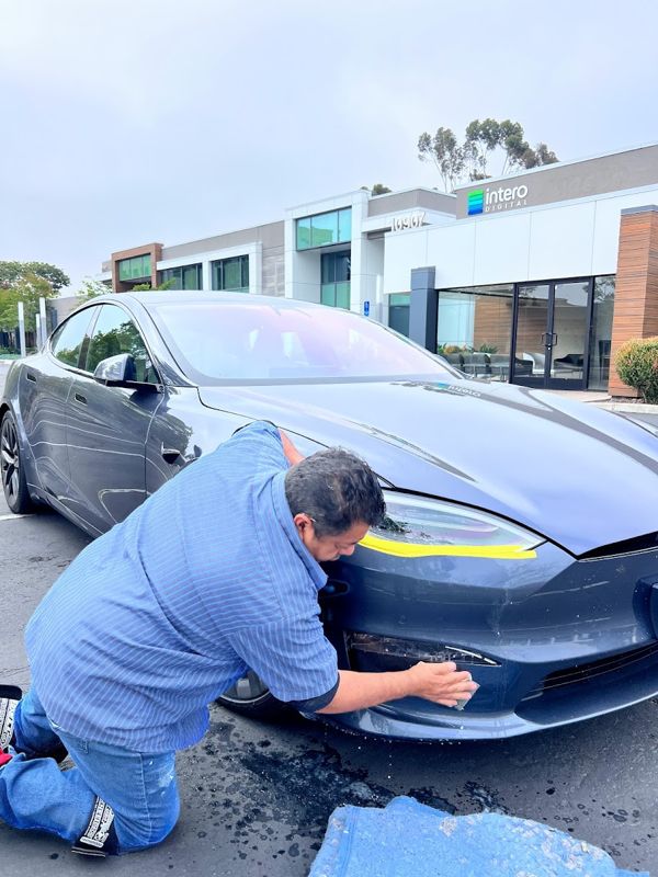 Technician hand-sanding a gray Tesla Model 3 bumper